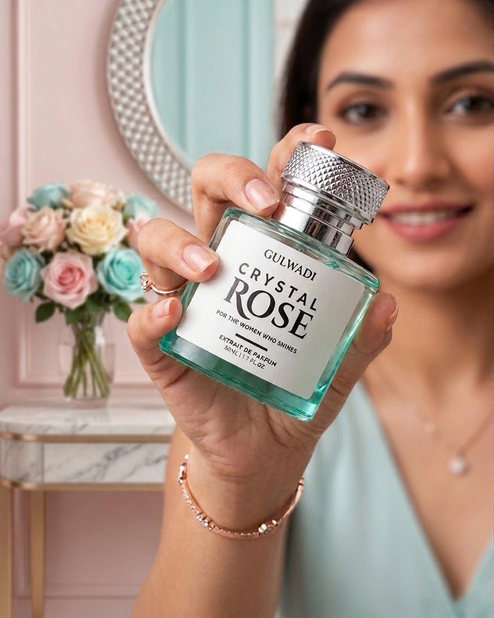 A woman holding a turquoise bottle of Gulwadi Crystal Rose Extrait de Parfum with a mirror and floral arrangement in the background
