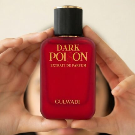 Hands holding a red matte bottle of Gulwadi Dark Poison Extrait de Parfum against a soft neutral background.