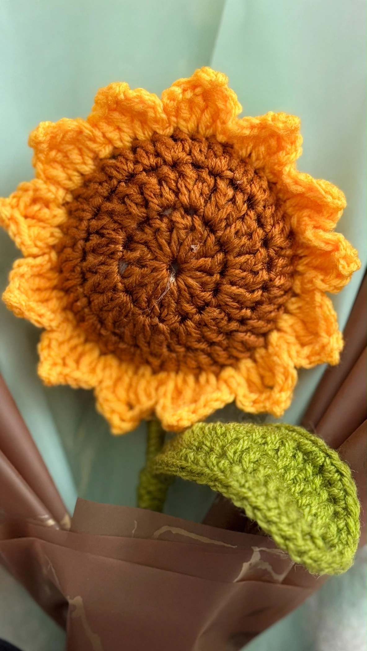 Close-up of the handmade crochet sunflower showing its stitched petals, brown crocheted centre and green leaf