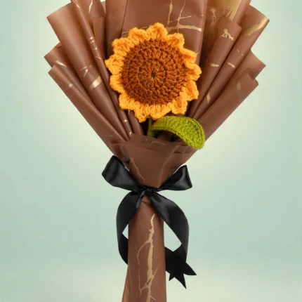 Handmade crochet sunflower bouquet in brown and gold wrapping with black ribbon on a mint green studio background