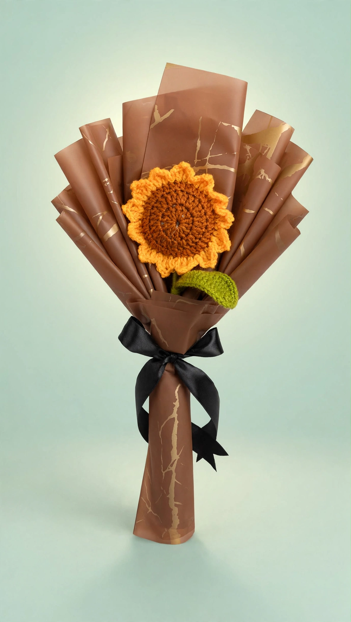 Handmade crochet sunflower bouquet in brown and gold wrapping with black ribbon on a mint green studio background