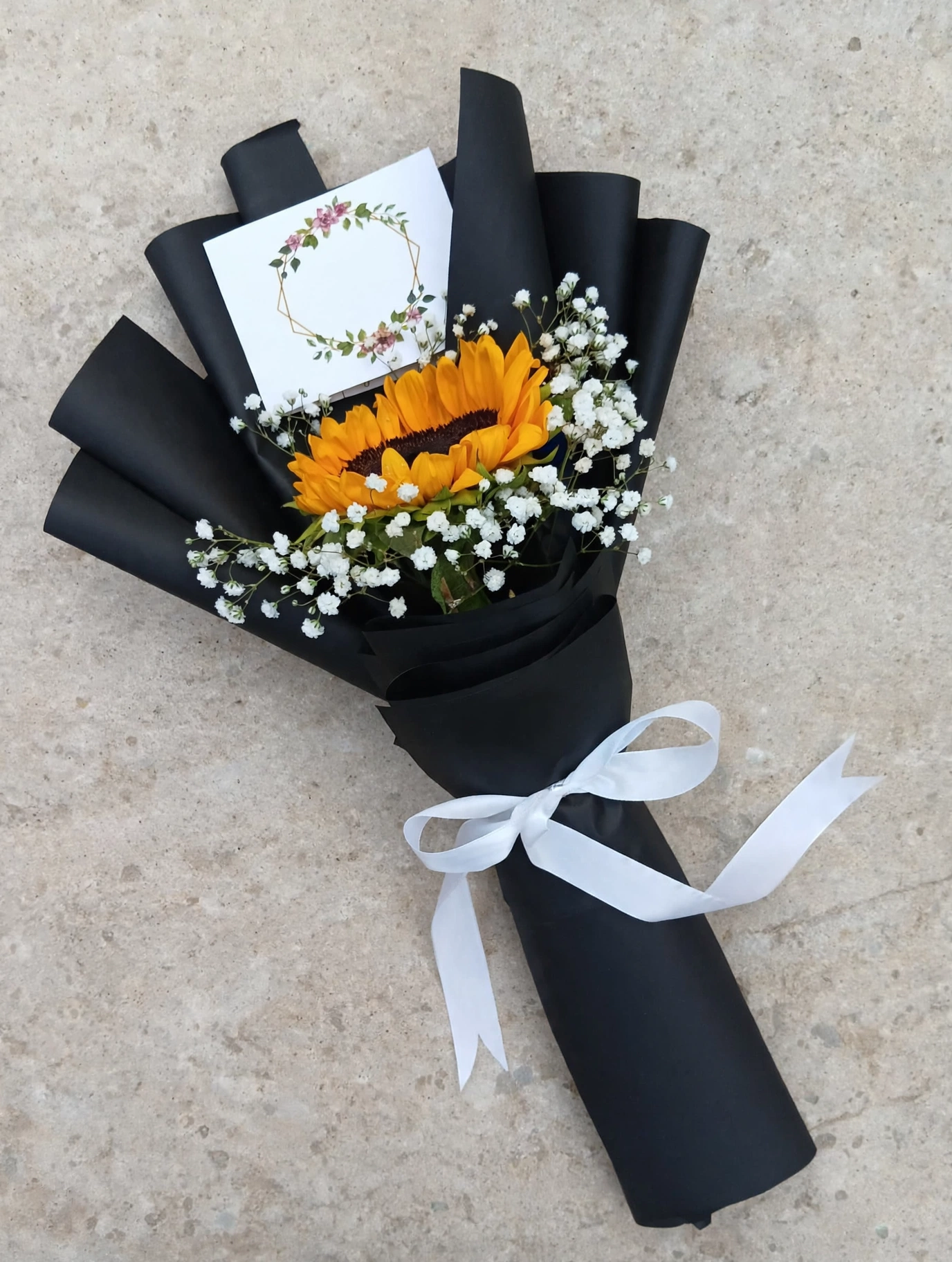 Single sunflower bouquet flat lay on a warm grey stone surface