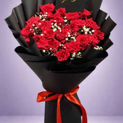 Sorry red rose bouquet with message card in tall black wrapping with red ribbon on a lavender studio background